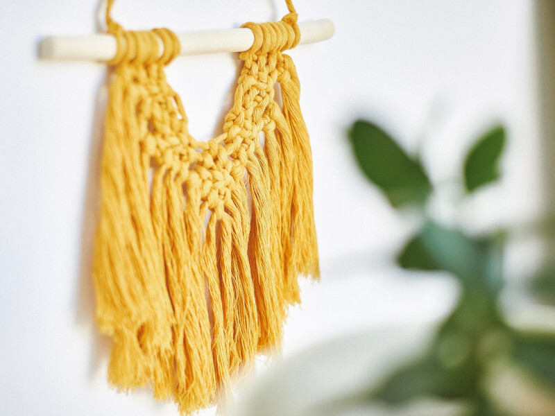 a yellow macrame wallhanging is displayed on a wall